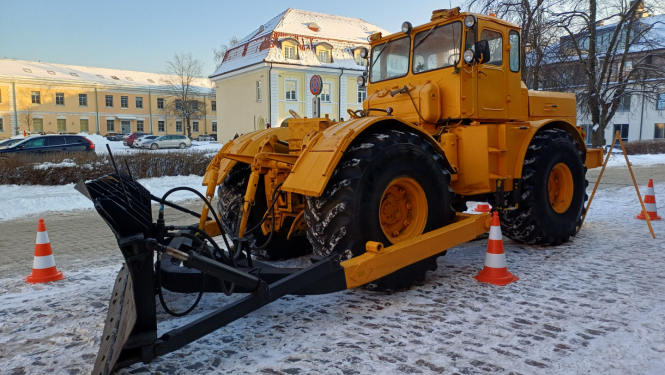 Liels dzeltens traktors ar lāpstu sniegotā pilsētvidē
