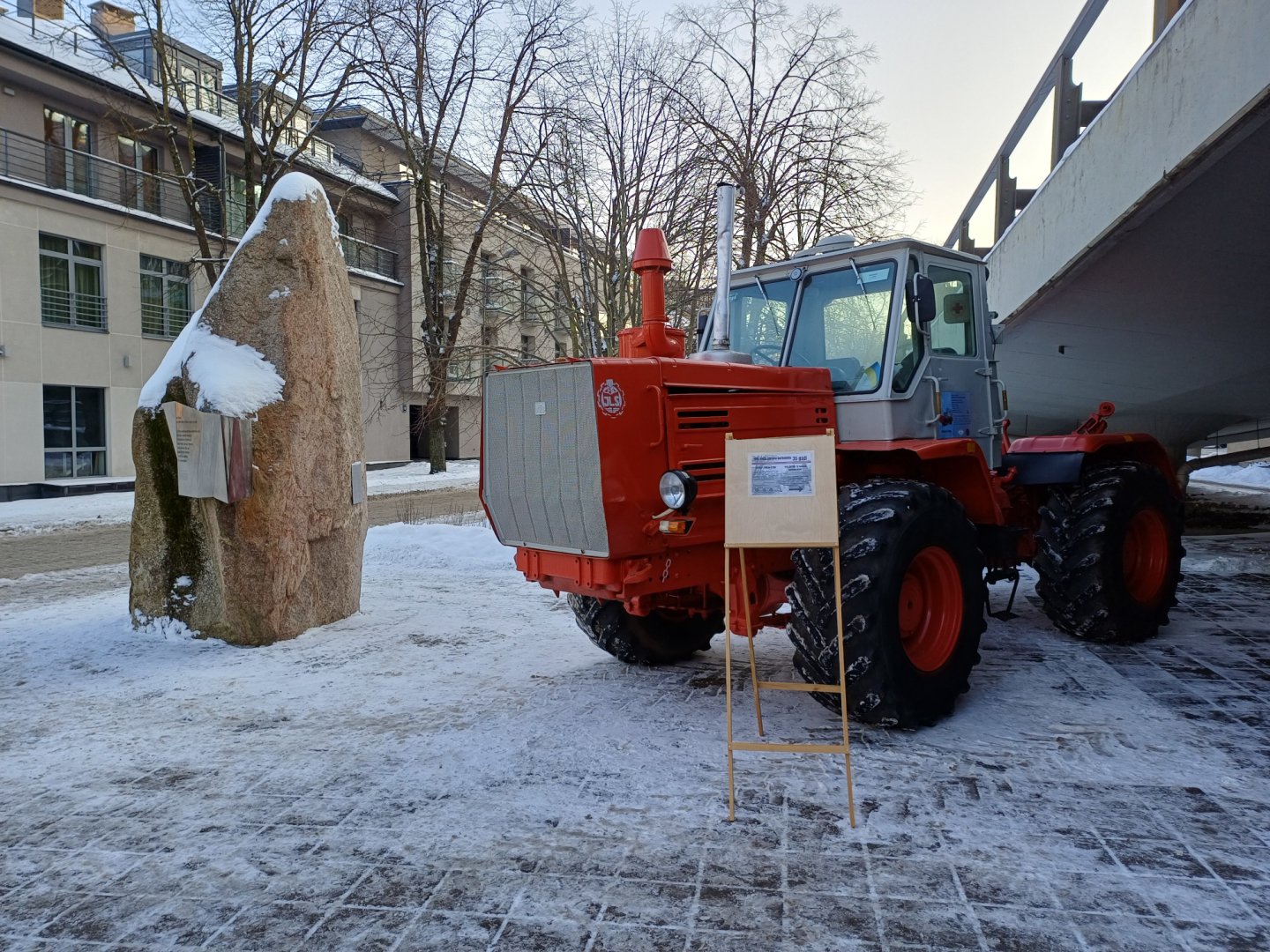 Sarkans traktors sniegotā pilsētvidē