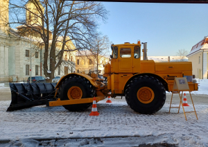 Liels dzeltens traktors ar lāpstu sniegotā pilsētvidē