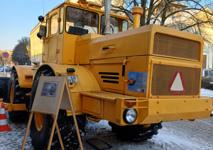Liels dzeltens traktors ar lāpstu sniegotā pilsētvidē