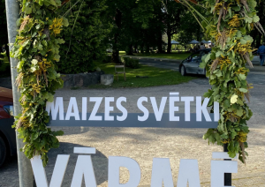 Dabas materiāliem izrotāts uzraksts maizes svētki Vārmē. Fonā bruģēts ieejas laukums parkā, pasākuma norises vietā