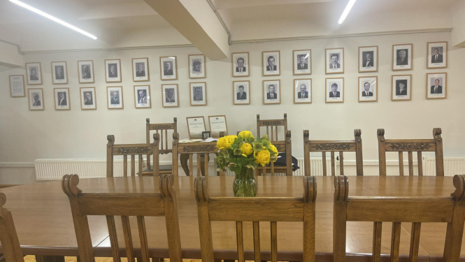 Kabinets (telpa) ar lielu galdu un krēsliem. Uz galda vāzē dzeltenas puķes, pie sienas Latvijas Republikas zemkopības ministru foto galerija.