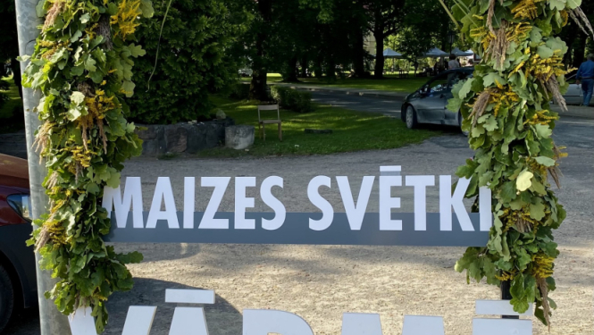 Dabas materiāliem izrotāts uzraksts maizes svētki Vārmē. Fonā bruģēts ieejas laukums parkā, pasākuma norises vietā