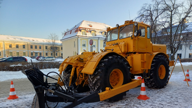 Liels dzeltens traktors ar lāpstu sniegotā pilsētvidē