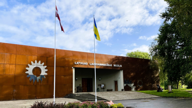 Latvijas Lauksaimniecības muzeja ēkas ieejas skats, ar diviem plīvojošiem karogiem