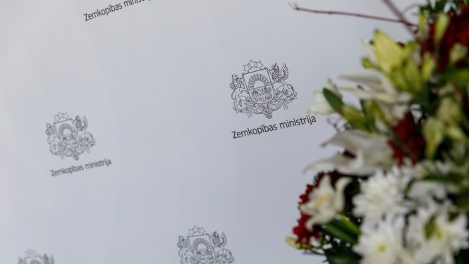 Fonā Zemkopības ministrijas nosaukums atkārtojas uz balta fona. Labajā pusē nedaudz aizmiglots puķu pušķis.