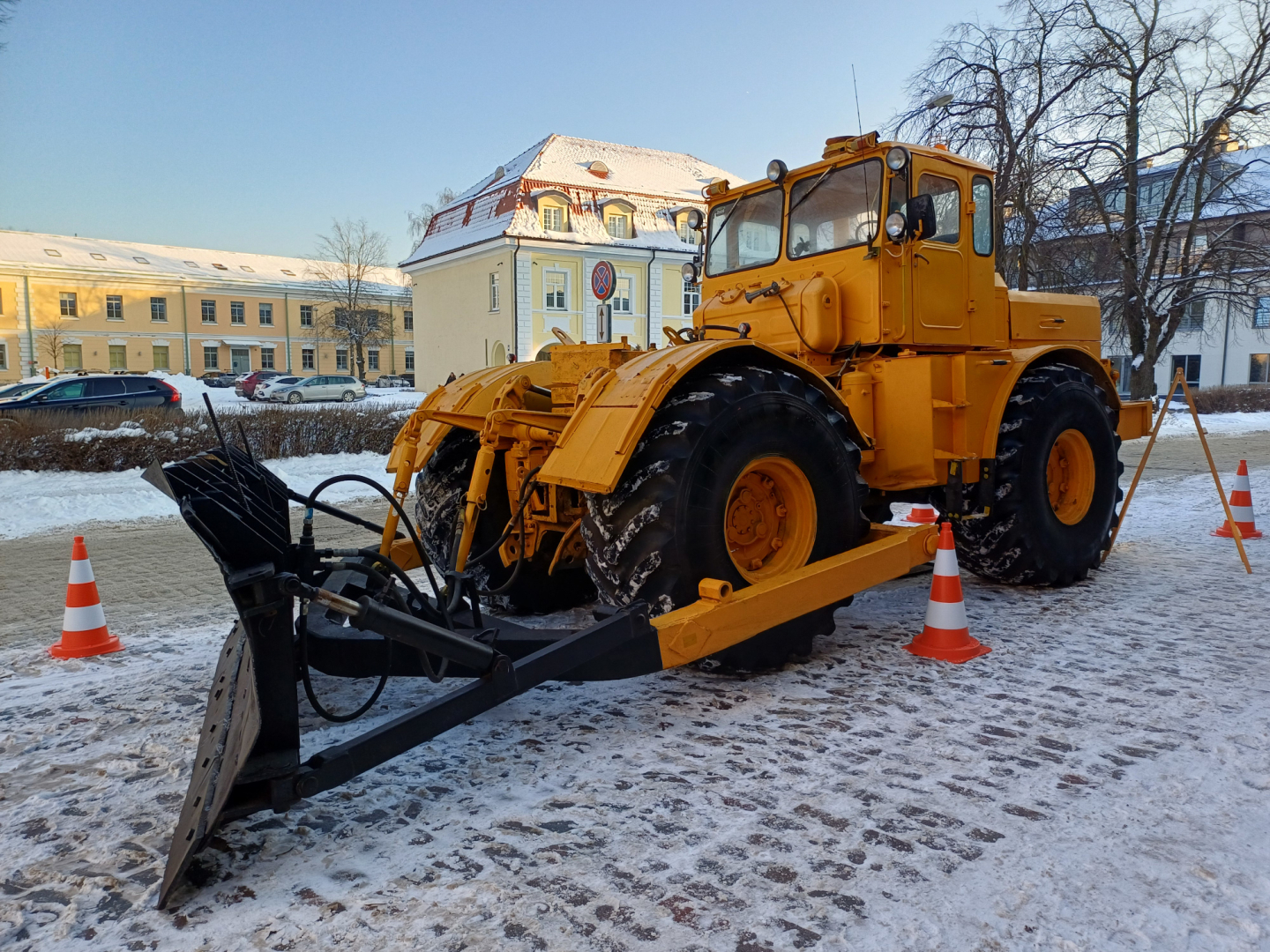 Liels dzeltens traktors ar lāpstu sniegotā pilsētvidē