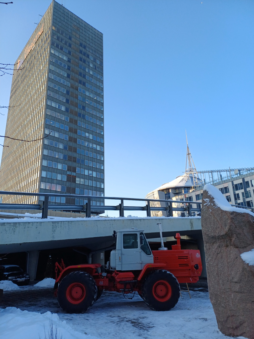 Sarkans traktors sniegotā pilsētvidē