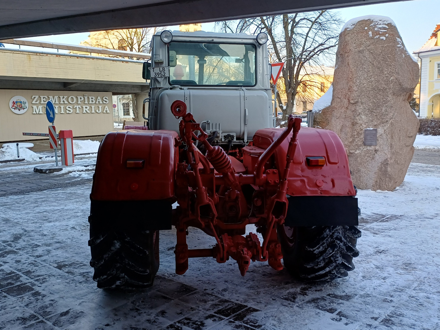 Sarkans traktors sniegotā pilsētvidē