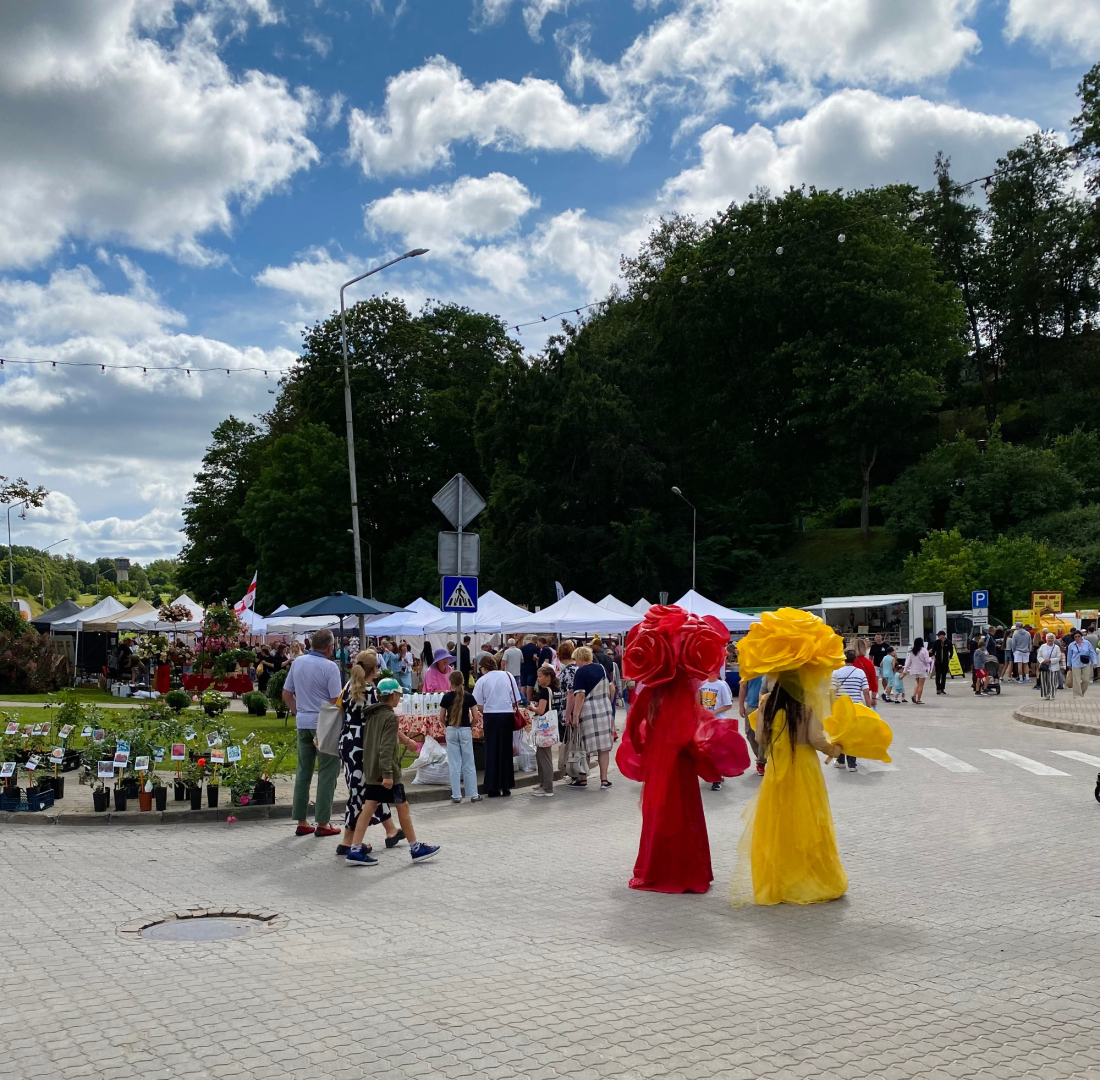 Ielas skats. Gadatirgus apmeklētāji un dzīvas, krāsainas ziedu skulptūras dodas savās gaitās tirgū