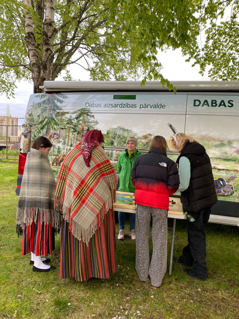 Piecas sievietes sastājušas pie mobilās dabas klases stenda Muzeju nakts pasākuma laikā