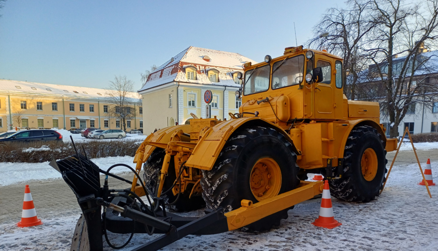 Liels dzeltens traktors ar lāpstu sniegotā pilsētvidē