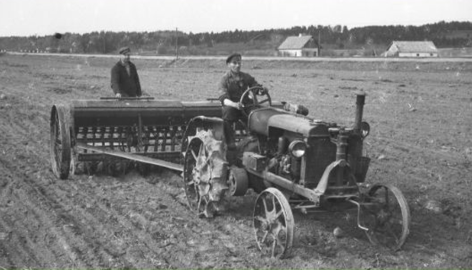 Muzeja izstādes informatīvais stends. Vidū bilde - senlaicīgs traktors velk sējmašīnu, kurā sēklu regulē cilvēks. Fons zaļos toņos, zāle tuvplānā.